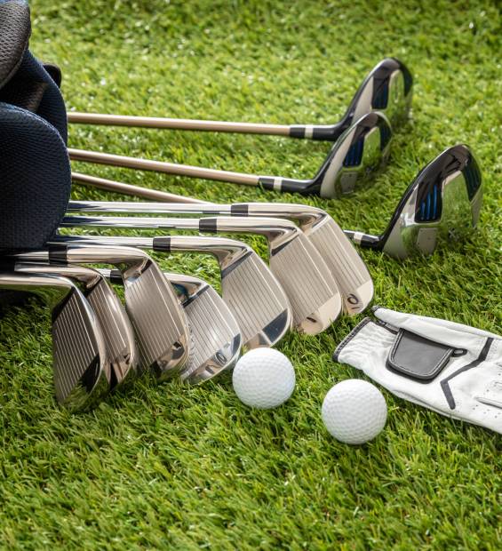 Golf equipment, sticks set in a bag glove and golfballs on green course lawn, close up vertical view. Golfing sport and club concept